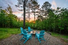 a group of blue chairs sitting on top of a gravel covered field next to trees