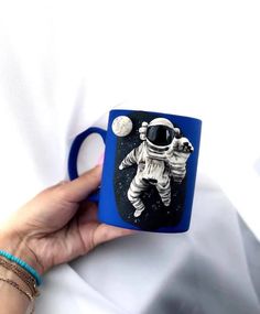 a hand holding a coffee mug with an astronaut on it