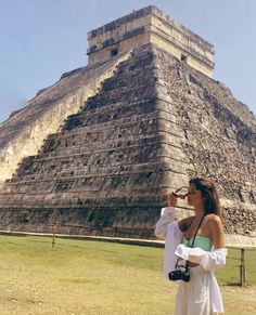 a woman standing in front of an ancient pyramid drinking from a glass with her hand