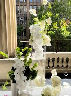 white flowers and greenery are arranged in vases on a table near a balcony