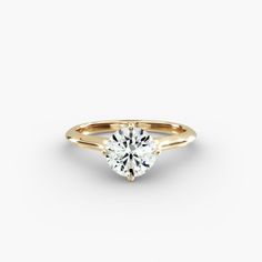 a yellow gold engagement ring with a round brilliant cut diamond in the center, on a white background