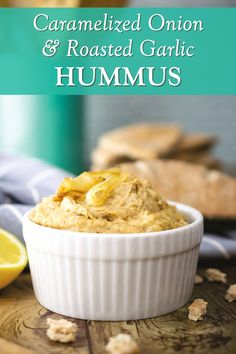 a white bowl filled with hummus next to sliced lemons and crackers on a wooden table