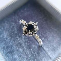 a black diamond ring sitting on top of a blue velvet covered box with silver accents