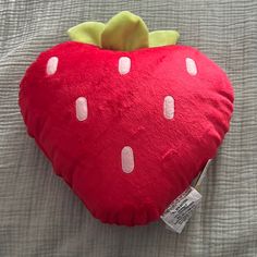 a red strawberry shaped pillow with white polka dots on it's side, sitting on a bed