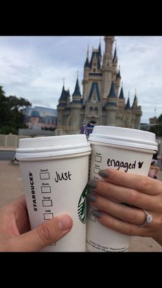 two people holding up coffee cups in front of a castle