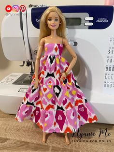 a doll is standing next to a sewing machine with a pink and yellow dress on it