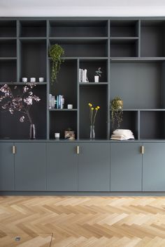 an empty room with shelves, vases and flowers on the floor in front of it