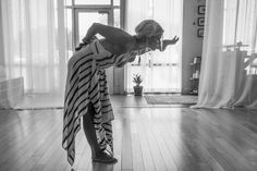 a woman standing on top of a wooden floor in front of a window with curtains