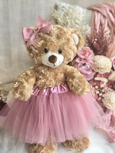 a brown teddy bear wearing a pink tutu skirt and sitting on a white couch