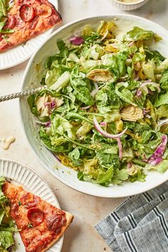 two plates with slices of pizza on them next to a bowl of lettuce