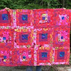 a person holding up a colorful quilt in front of some trees