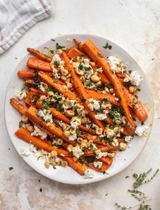 a white plate topped with carrots covered in feta and pine nuts next to a towel