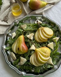 a salad with pears and greens on a plate next to two glasses of juice