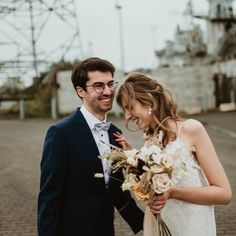 a man and woman standing next to each other in front of an industrial area with power lines