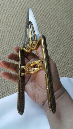 a pair of scissors that are sitting in someone's hand with gold trimmings