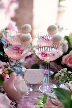 two wine glasses filled with candy sitting on top of a table next to pink flowers