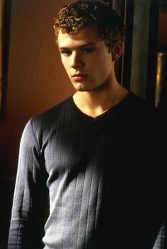 a young man with curly hair standing in front of a door wearing a black sweater