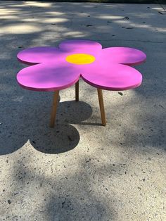 a pink flower shaped table sitting on top of a cement ground next to a tree