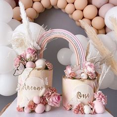 two cakes decorated with flowers and feathers are sitting on a table in front of balloons