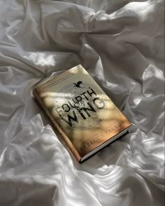 a book sitting on top of a bed covered in white sheets and satin material with the words fourth wing written across it