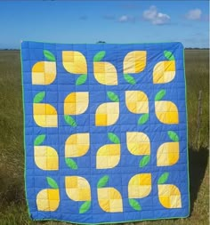 a blue and yellow quilt with lemons on it in the grass near a fence