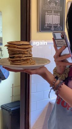 a woman holding up a stack of pancakes on top of a plate with a cell phone in her hand