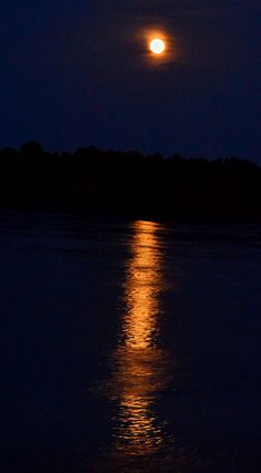 the full moon shines brightly in the night sky above water's surface as it reflects its reflection