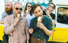 two men eating ice cream while standing in front of a yellow van with other people