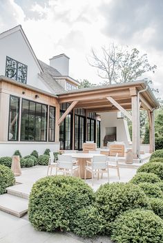 an outdoor dining area in front of a house with large windows and wooden pergols