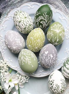 some green and white decorated eggs on a plate with flowers in the backgroun