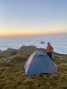 a man standing next to a tent on top of a mountain