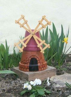 a statue of a windmill made out of clay and wood sticks in the ground next to flowers