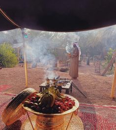 a person standing next to a large pot filled with food on top of a rug