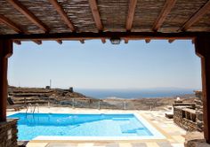 an outdoor swimming pool surrounded by stone walls and wooden beams with the ocean in the background