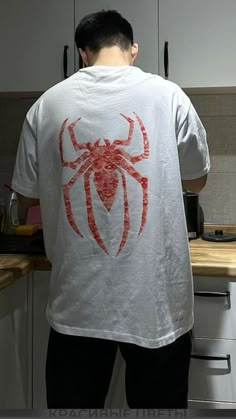 a man standing in a kitchen wearing a spiderman t - shirt on his back