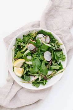 a white bowl filled with spinach and radishes on top of a table