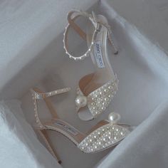 a pair of white high heeled shoes in a box with pearls on the heels