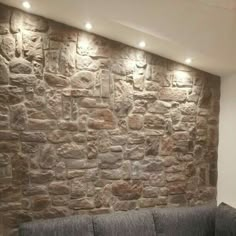 a living room with a couch and stone wall in the corner, along with recessed lighting