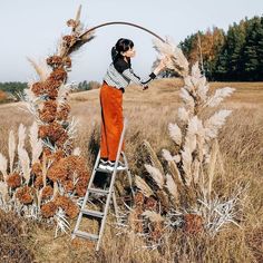 a woman is standing on a ladder in the middle of a field with tall grass