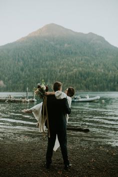 a man holding a woman on his back while standing next to a body of water