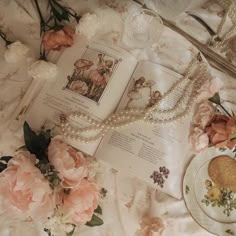 an open book with pearls and flowers surrounding it on a table cloth next to a plate