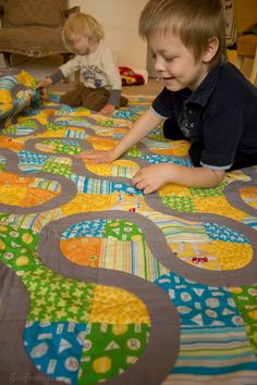 two young boys playing on the floor with colorful quilts and pillows in front of them