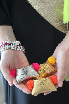 the woman is holding three pieces of gold and silver jewelry with pom - poms