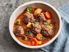 a white bowl filled with meatballs, carrots and potatoes next to a blue towel