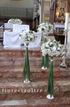 three bouquets of white flowers sit on the steps in front of a church pew