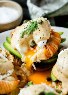 a white plate topped with an open face sandwich and cucumber slices covered in cream sauce