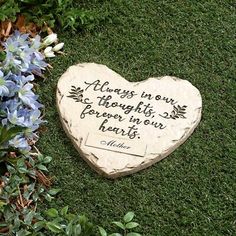 a heart shaped stone with a quote on it sitting in the grass next to blue flowers