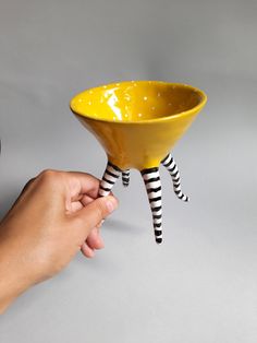 a hand holding a yellow bowl with black and white striped legs on the bottom, while another hand holds it up