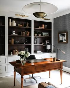 a desk with flowers and books on it in front of a bookcase full of books