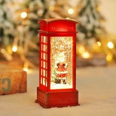 a red phone booth sitting on top of a snow covered ground next to a christmas tree